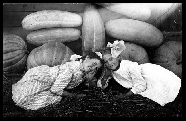 Two girls with pumpkins, squash, and watermelons