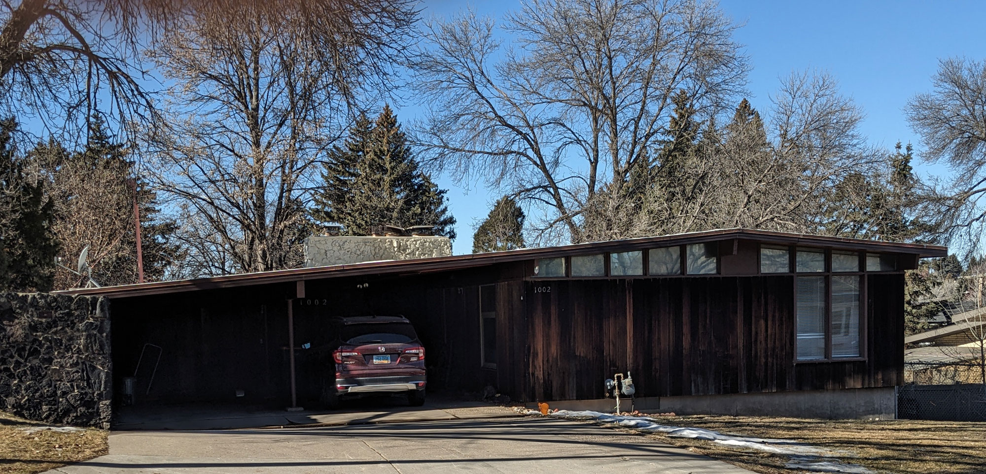 A brown house with the roof extending over a garage or car port.