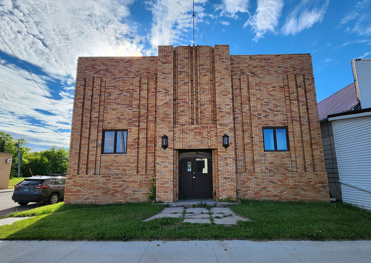 Multicolored tan, orange, and brown brick building with a double window and light fixtures on both sides of the black door.