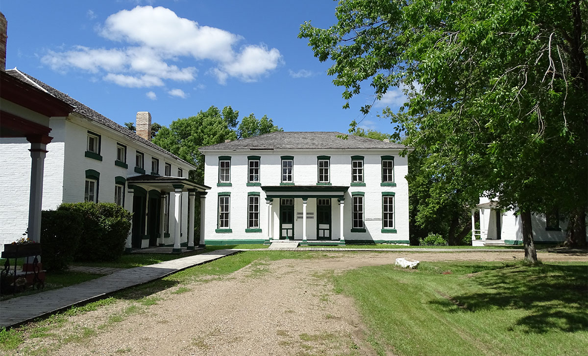 White wooden building with green trim around windows and doors and a gray roof.