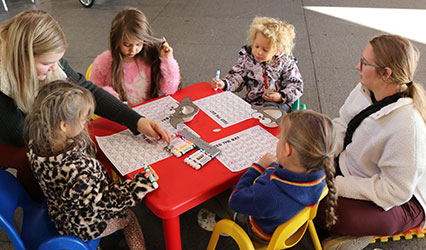 A group of toddlers and adults sit around a little, red table coloring sheets about bats