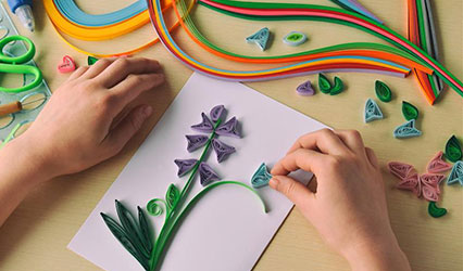A person is folding different colors of paper and putting them on a white sheet of paper to make flowers.
