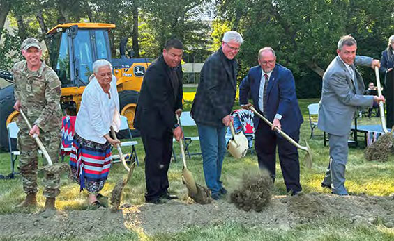 A group of people with shovels dig into a dirt pile for a groundbreaking ceremony